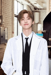a young man wearing a lab coat and tie is standing in a room .