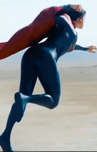 a woman in a superman costume is running on a beach .