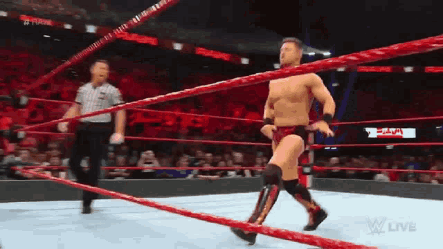 a man in a wrestling ring with a referee and a sign that says w live