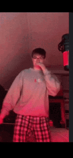 a man wearing a grey sweatshirt and plaid shorts is standing in a dark room