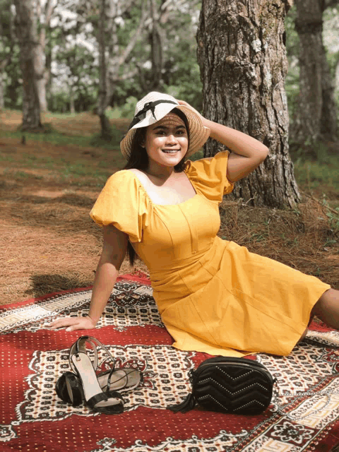 a woman in a yellow dress sits on a blanket in the woods