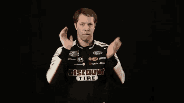 a man wearing a discount tire shirt is making a gesture