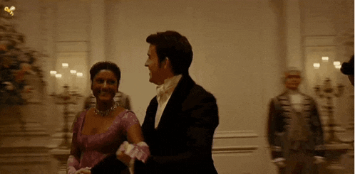 a man in a tuxedo and a woman in a pink dress are dancing in a ballroom .