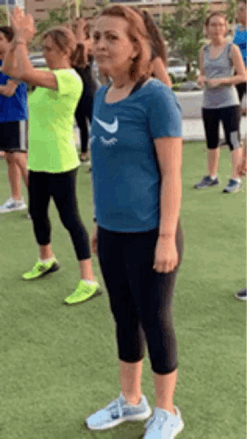 a woman in a blue nike shirt is standing in front of a group of people on a grassy field .