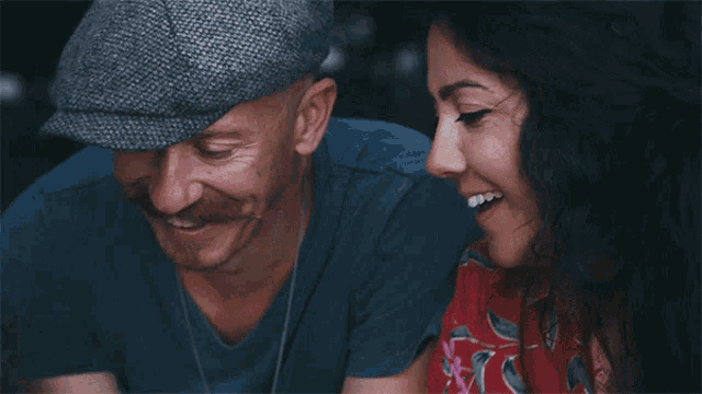 a man wearing a hat is smiling next to a woman in a red shirt