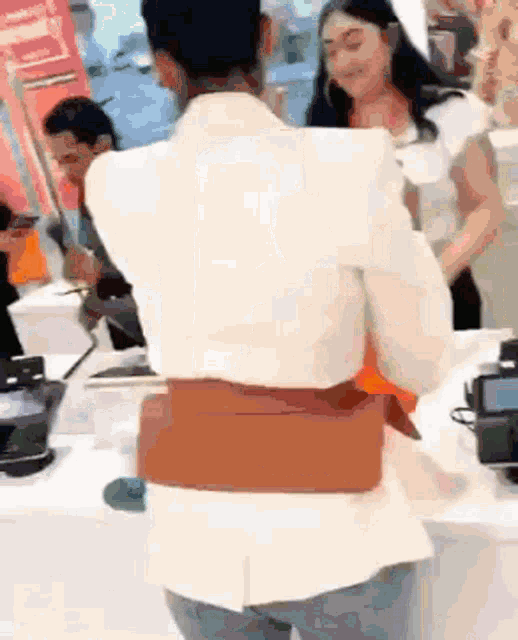 a woman wearing a white jacket and a brown belt is standing in front of a counter in a store