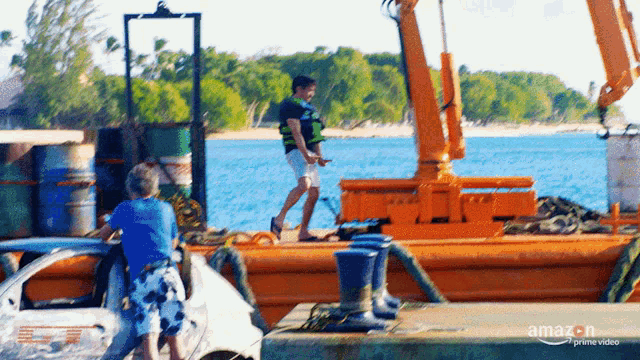 a man is standing on a dock next to a large orange boat .