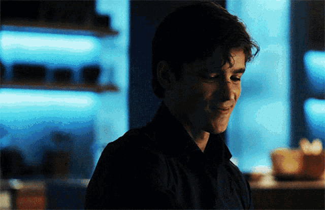 a man in a black shirt is smiling in a dark room with blue lights