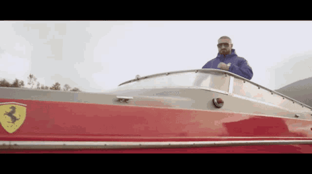 a man in a blue jacket is driving a red boat with a ferrari logo on it