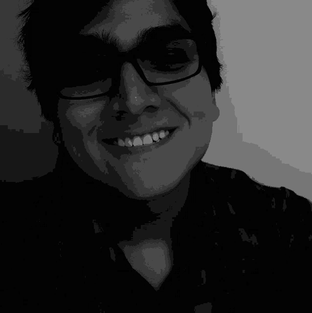 a young man wearing glasses and a plaid shirt smiles in a black and white photo