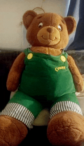 a brown teddy bear wearing green overalls with the word corduroy on the chest