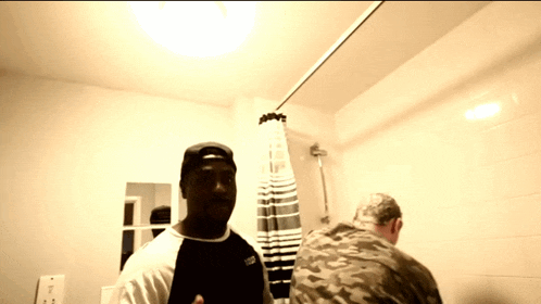 a man in a black and white shirt with the word vans on it stands in a bathroom