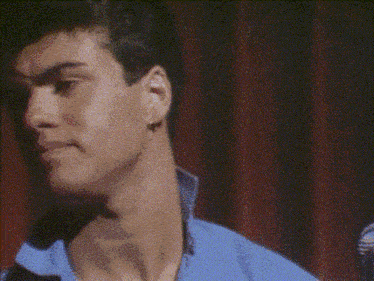 a man in a blue shirt holds a microphone in front of a red curtain