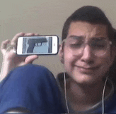 a man wearing glasses is taking a picture of himself with a gun on his phone .