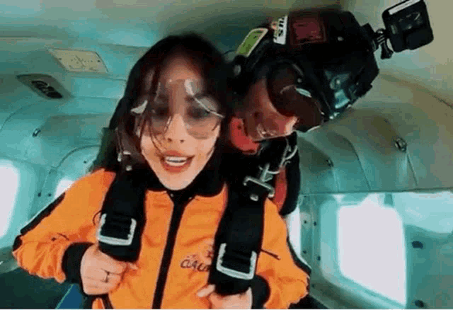 a woman in an orange jacket is being pulled by a man in a parachute
