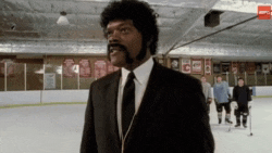 a man in a suit and tie is standing on an ice rink with hockey players in the background .