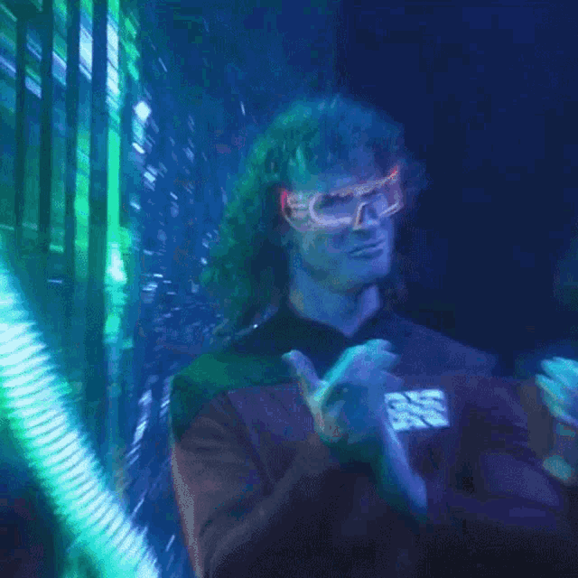 a man wearing glow in the dark goggles is clapping his hands in a dark room with a purple light behind him .