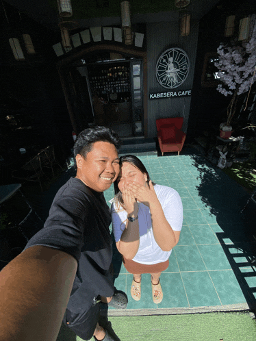 a man and woman pose for a photo in front of a kabesara cafe