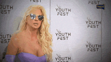 a woman wearing sunglasses is standing in front of a wall that says youth fest