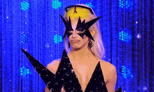 a drag queen is wearing a mask and holding a trophy on a stage .