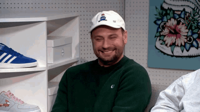 a man wearing a green sweater and a white hat is laughing