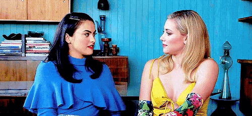 two women are sitting next to each other in front of a blue wall and talking to each other .