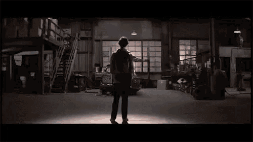 a man is standing in a dark room holding a car 's headlights .