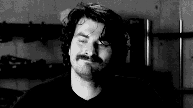 a black and white photo of a man with a mustache smiling .