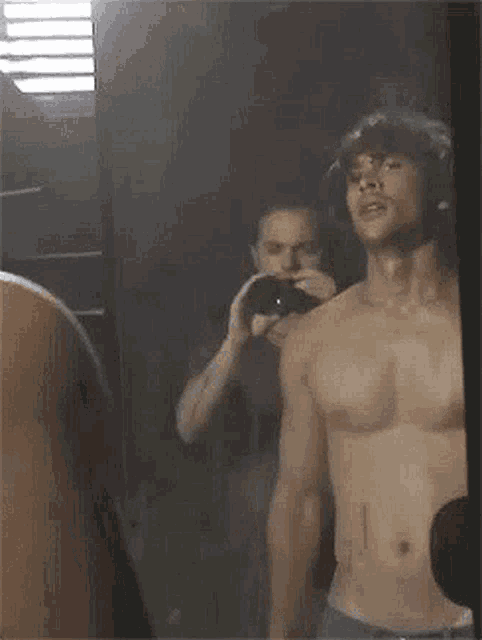 a shirtless man is taking a selfie in front of a mirror .