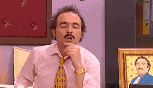 a man with a mustache is sitting in front of a framed picture of a man