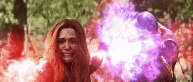 scarlet witch is crying while a man throws a purple and red smoke bomb at her .