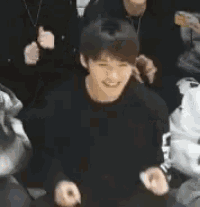 a man in a black sweater is smiling while sitting in a crowd of people .