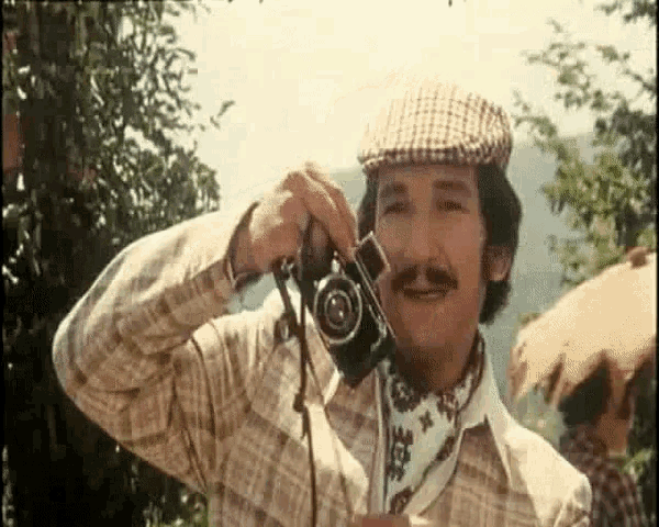 a man wearing a hat and scarf is holding a camera .