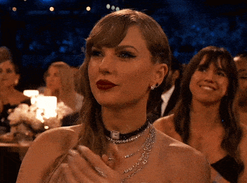 a woman wearing a choker and a necklace is clapping her hands in a crowd of people .