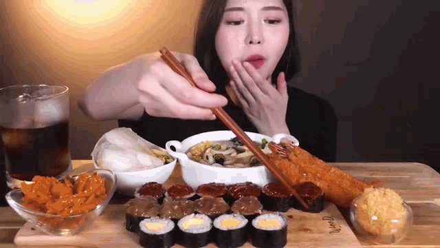 a woman is eating sushi with chopsticks on a wooden cutting board