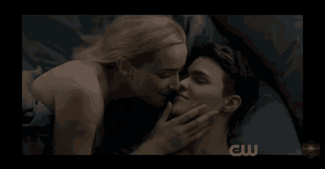 a couple kissing on a bed with a cw logo in the background