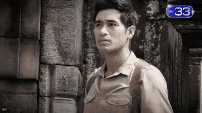 a black and white photo of a man standing in front of a brick wall .