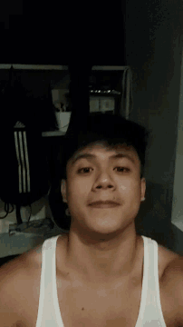 a man wearing a white tank top looks down at the camera