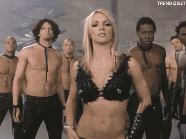 a woman in a black bra stands in front of a group of men with a sign that says keep clear