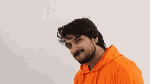 a man with a beard wearing an orange hoodie looks at the camera