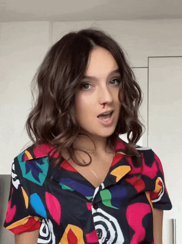 a woman wearing a colorful shirt has a bloody nose on her face