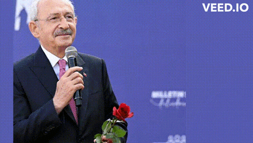 a man in a suit and tie is holding a red rose in front of a microphone with the words ben kemal geliyorum below him