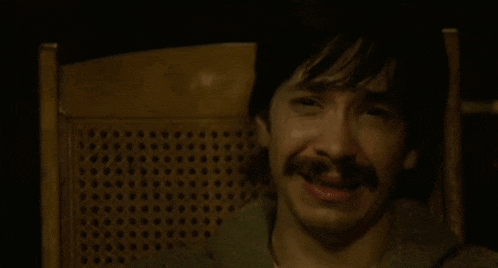 a man with a mustache is sitting in a chair and smiling .