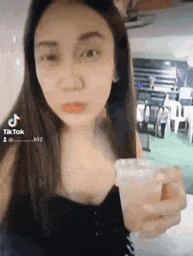 a woman is holding a cup of liquid in her hand and looking at the camera .