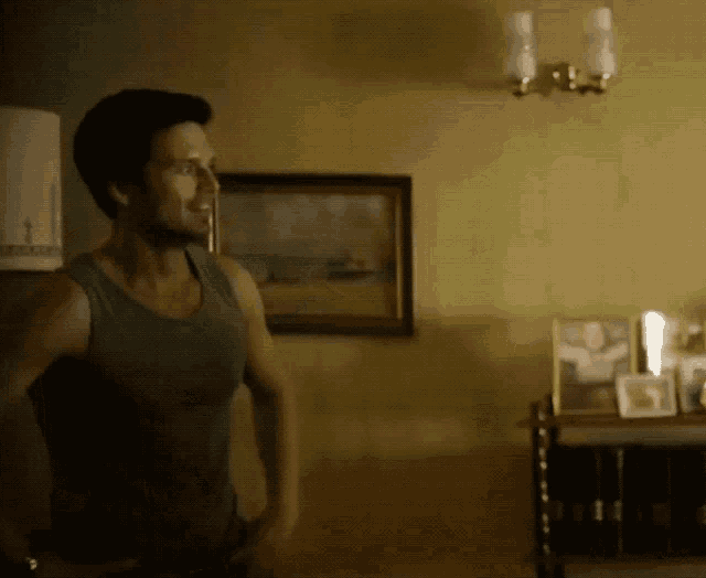 a man in a tank top is standing in a room with a picture on the wall