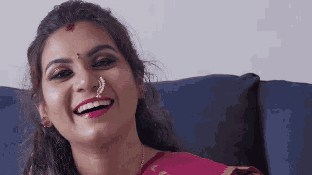 a woman with a nose ring is smiling and wearing a pink shirt