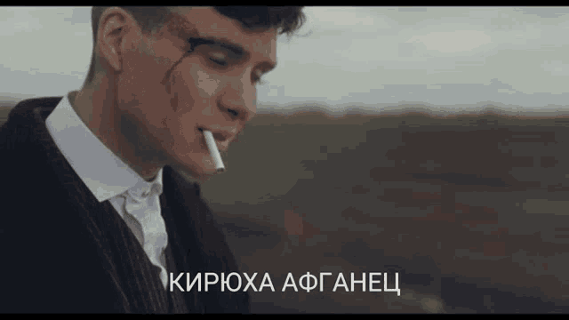 a man smoking a cigarette in a field with the words " кирюха афганец " written below him