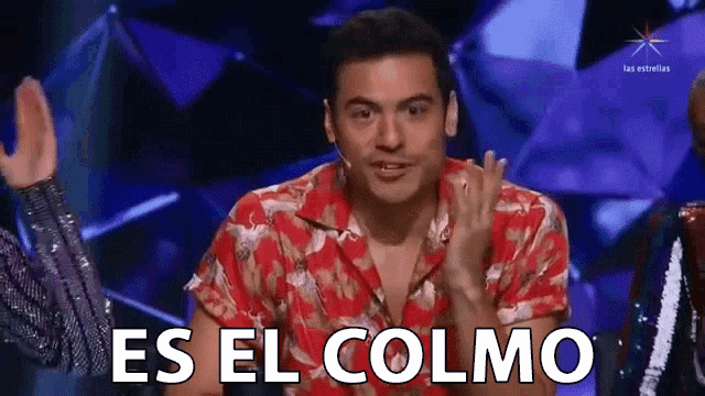a man in a red shirt is sitting on a stage and says es el colmo
