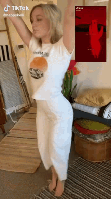 a woman in a white shirt and white pants is dancing in a room with a picture of a red hand in the background .