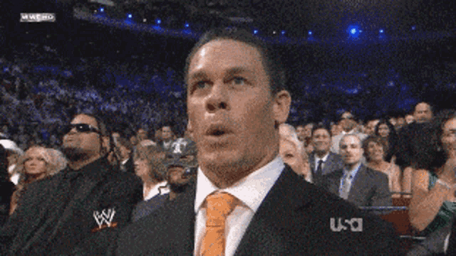 a man in a suit and tie is making a funny face while watching a wrestling match on usa network